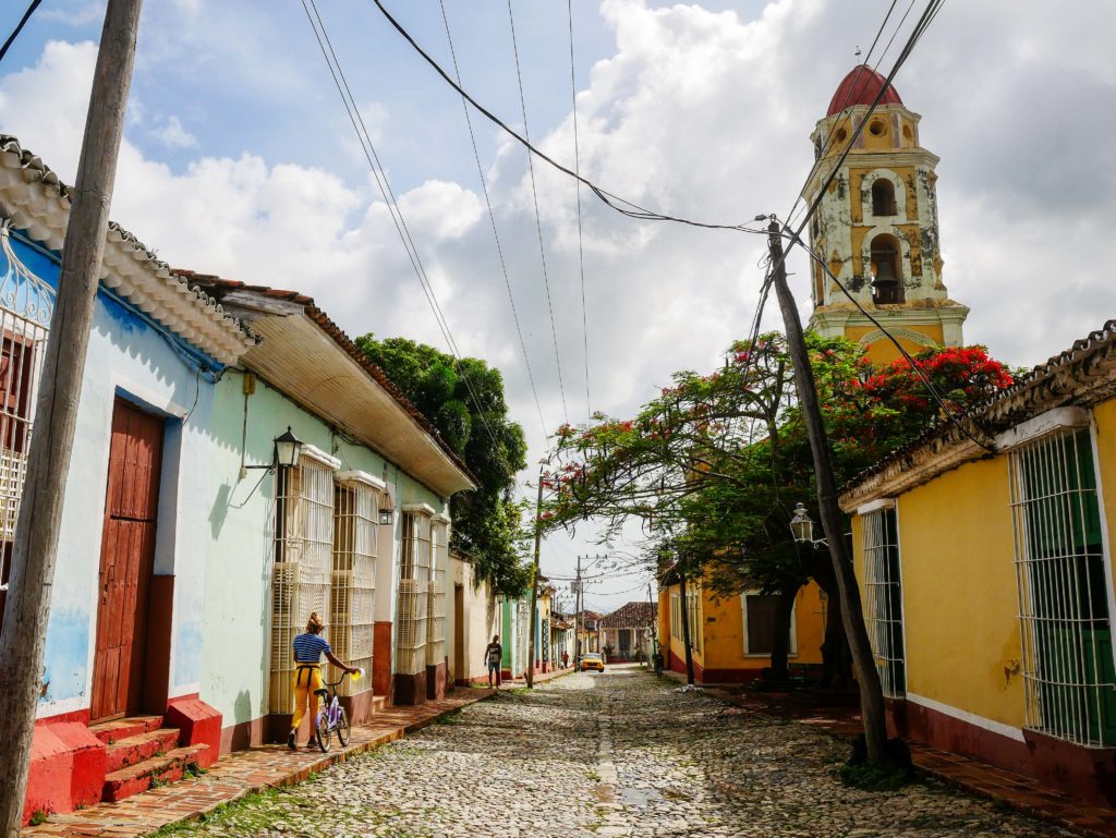 A quiet street in Trinidad, Cuba with pastel walls, cobblestones, and abell tower rising above