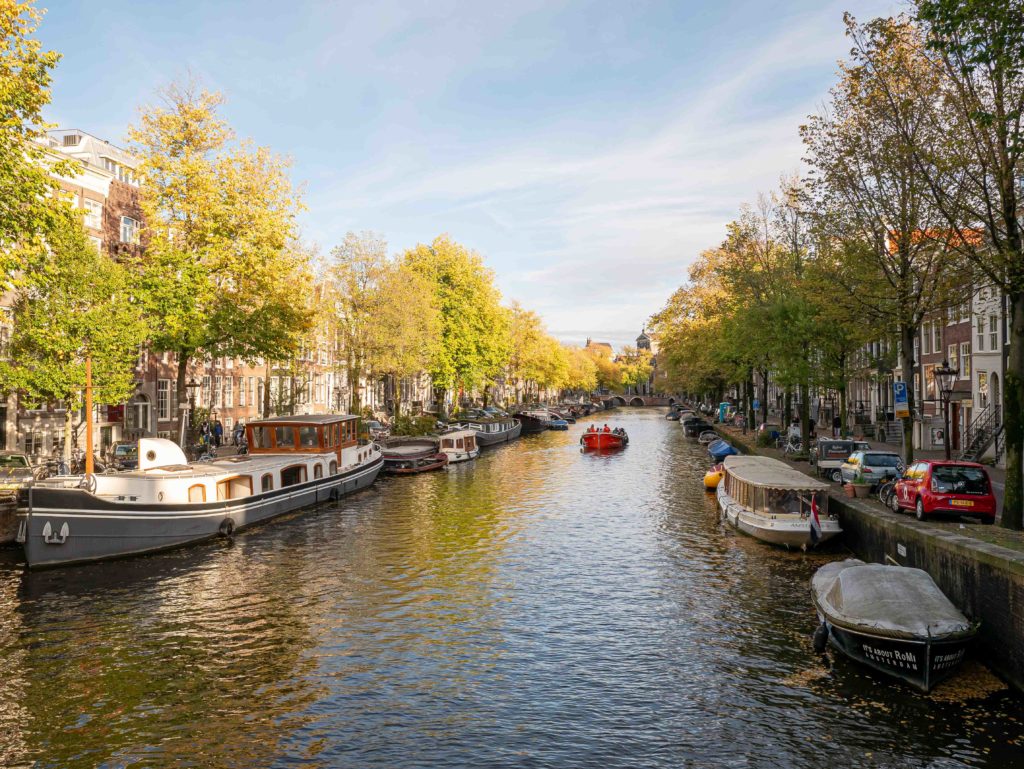 Golden light over Amsterdam’s canals with boats drifting between rows of autumn trees
