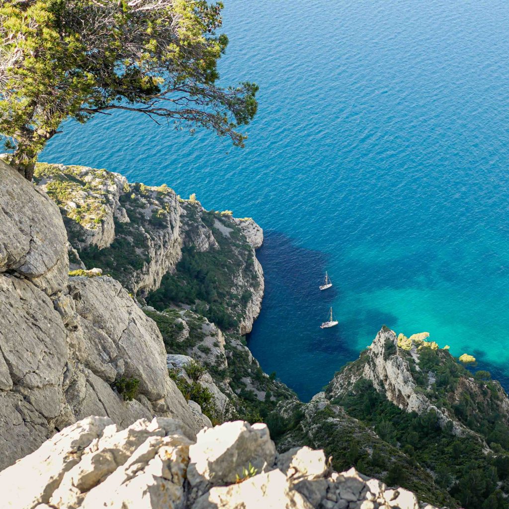 Sailboats anchored in the turquoise waters below the limestone cliffs of the Calanques near Marseille, France