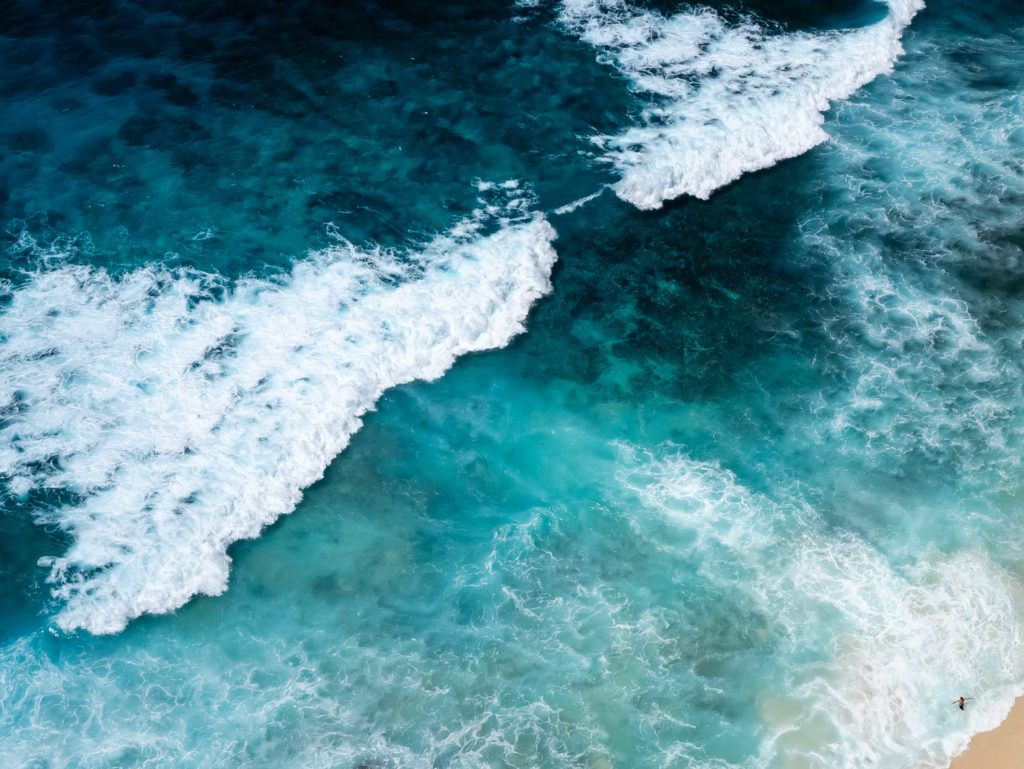 Aerial view of turquoise waves crashing along the shore in Nusa Penida, Indonesia