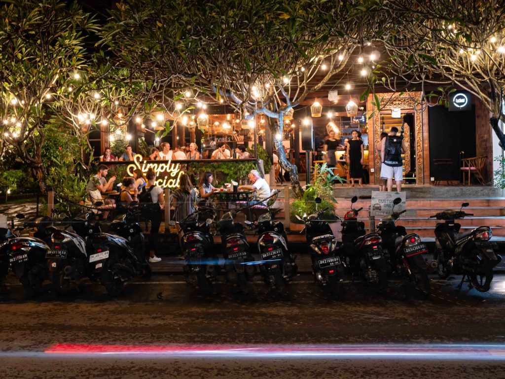 Night street view of a lively café with hanging lights and parked scooters in Ubud