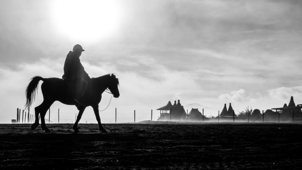 Silhouette of a horse rider at sunrise near Pura Luhur Poten temple in the Tengger Caldera