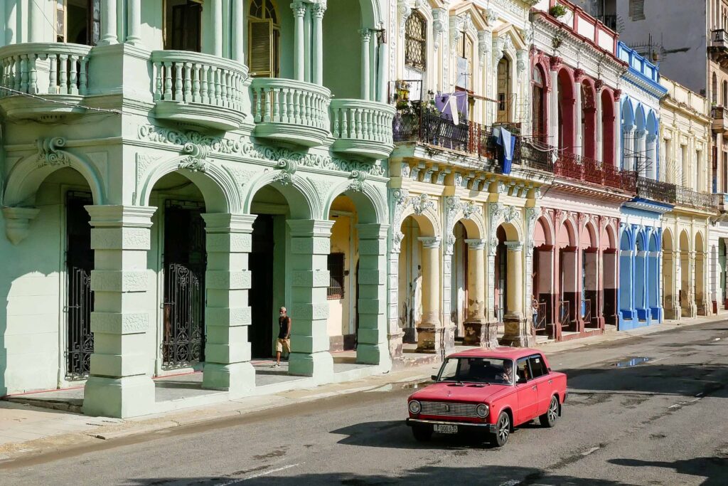 Old American car parked beside colorful colonial buildings in Havana
