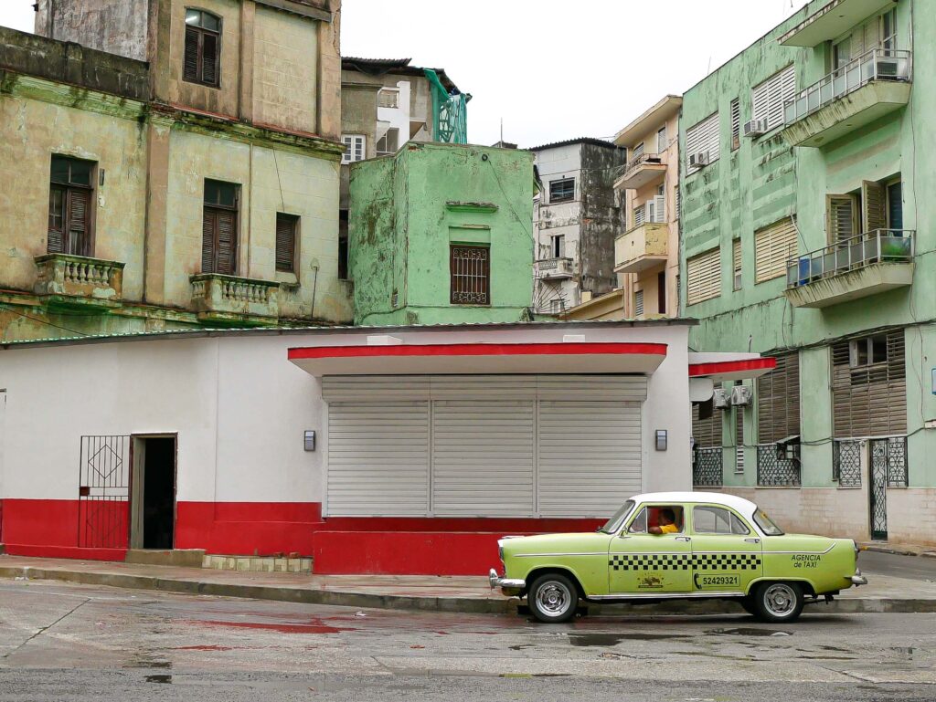 Vintage green American car parked beside weathered buildings in Havana